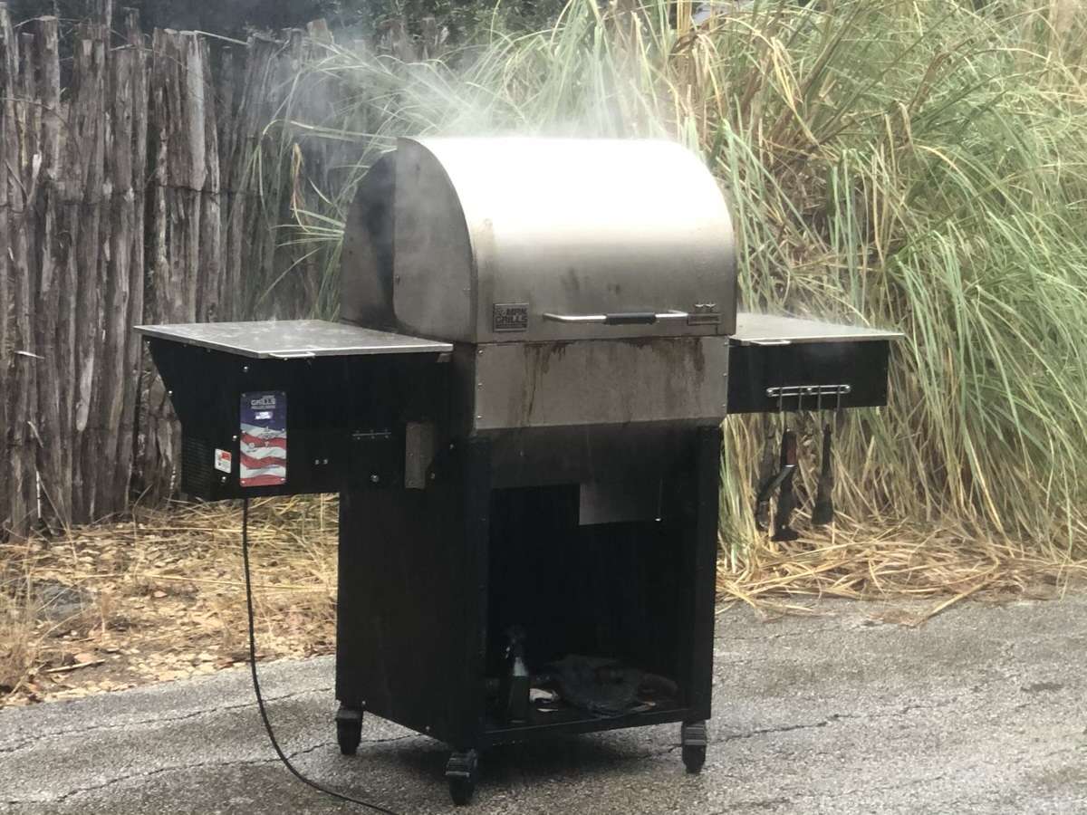 MAK 2 Star General pellet grill smoking three racks of baby back ribs as steam is rolling off the hood from the cold winter rain.