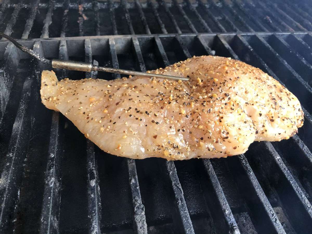 Seasoned chicken breast smoking on MAK 2 Star pellet grill with meat probe inserted.