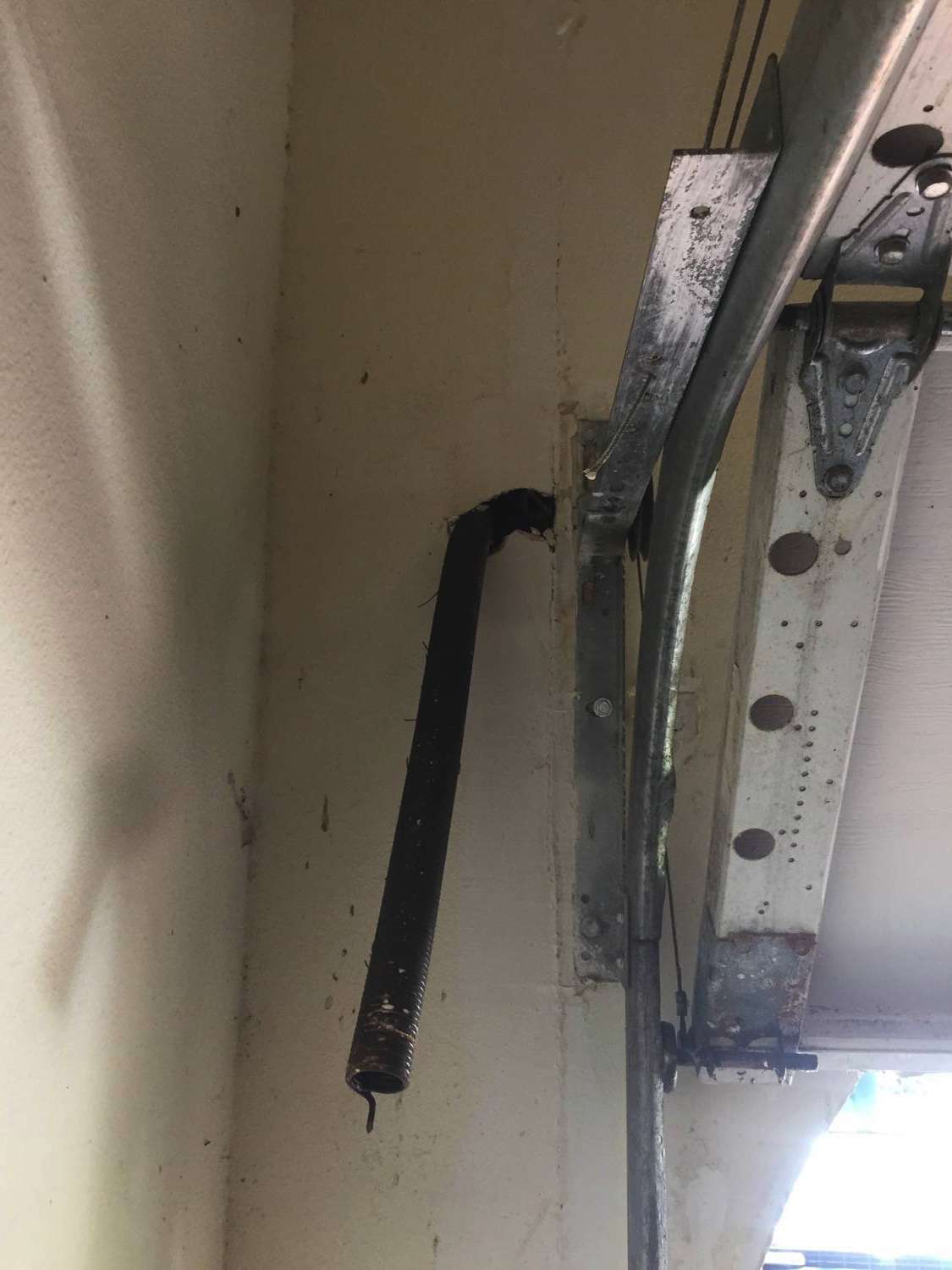Garage door extension spring sticking out of the sheetrock. The spring broke and it knocked a hole in the wall.